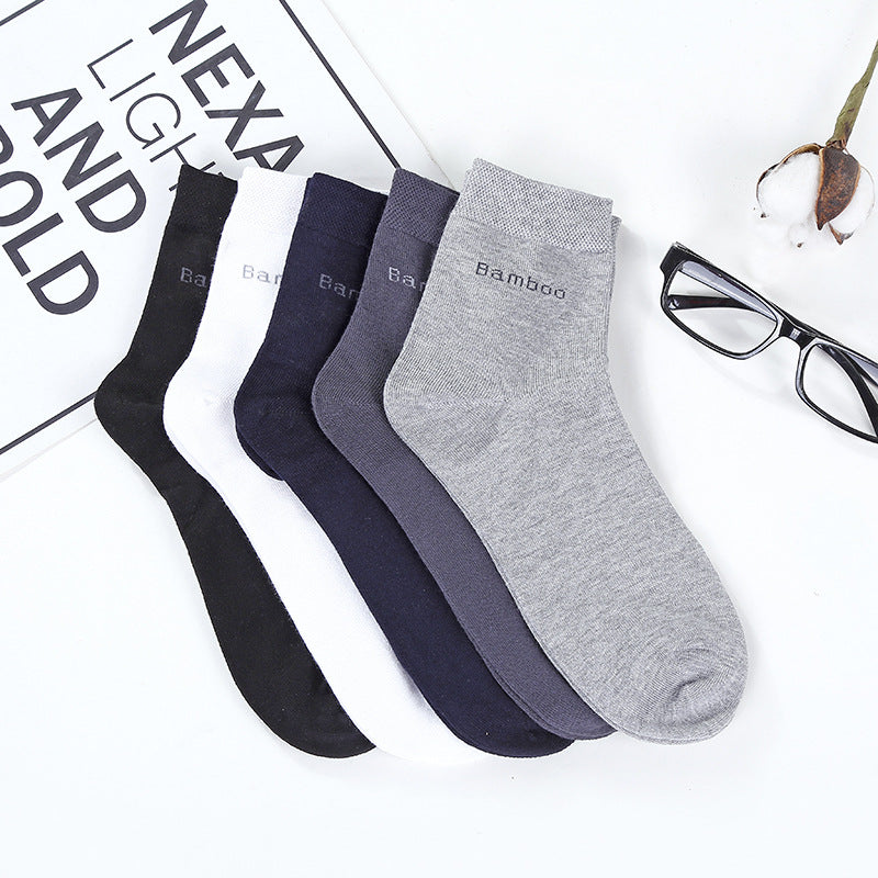 Four pairs of socks in black, navy, and gray on a newspaper background with glasses and a plant.