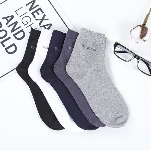 Four pairs of socks in black, navy, and gray on a newspaper background with glasses and a plant.